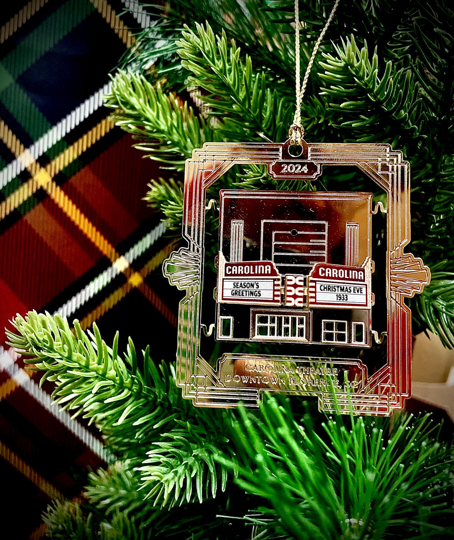 a gold christmas ornament featuring a historic theatre building against a red and green plaid background with spruce leaves